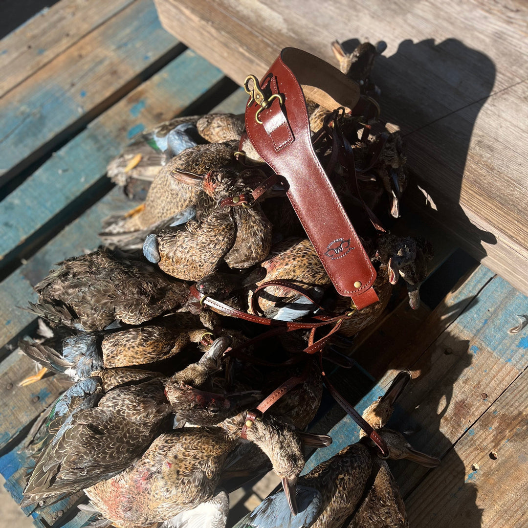 A pile of harvested teal ducks resting on a weathered blue wooden surface, with a reddish-brown leather strap or harness draped over the birds.