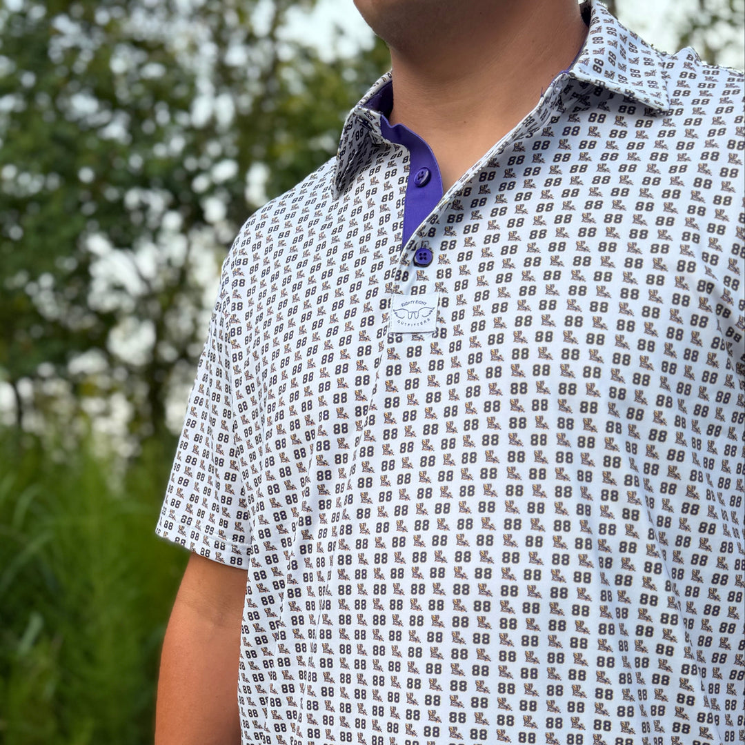 A man wearing a short-sleeve polo shirt with a repeating black and white geometric pattern and a purple inner collar, standing outdoors in a grassy area.
