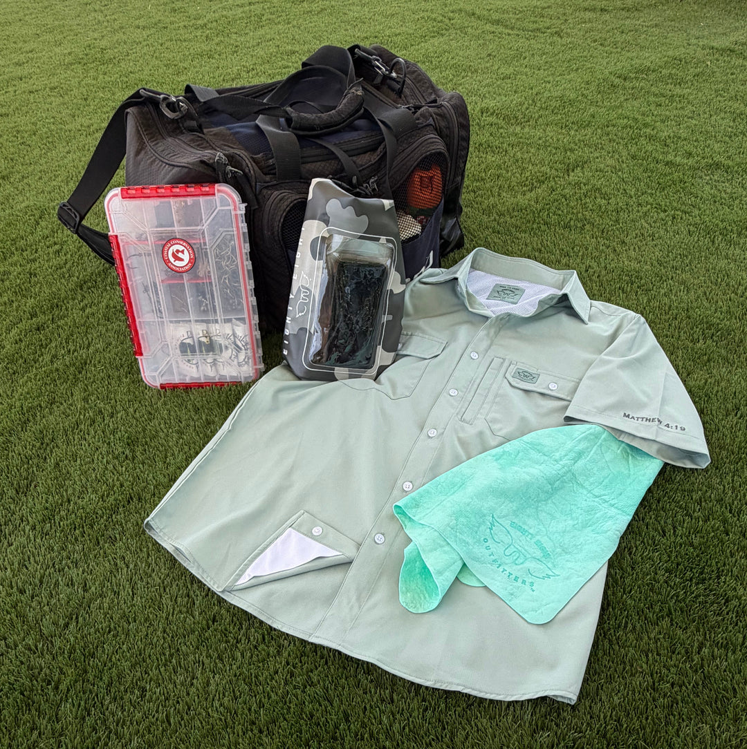 A golf course uniform kit laid out on green grass, including a light sage green short-sleeve button-up shirt, a mint green towel, a black duffel bag, a red and clear plastic utility case, and a packaged black glove.