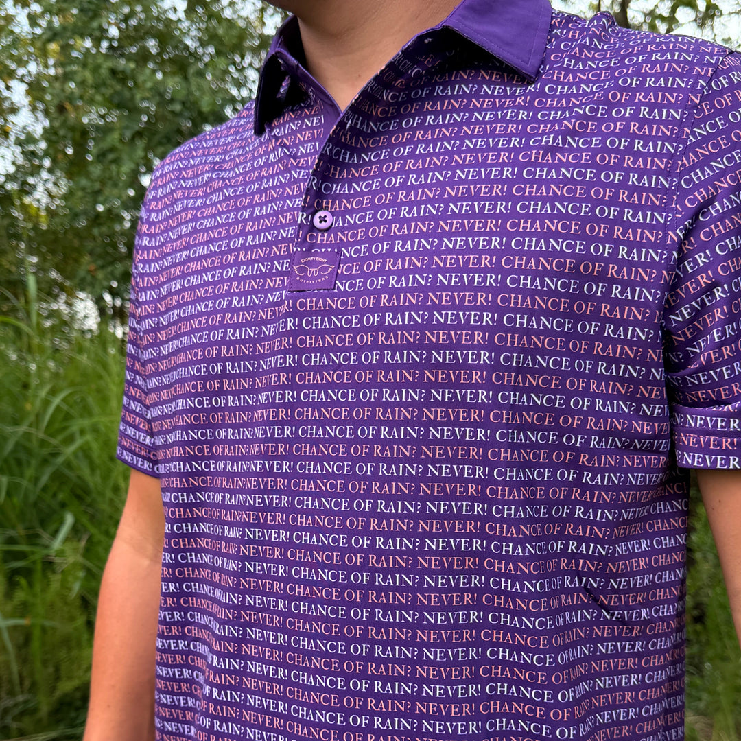 A close-up of a person wearing a purple short-sleeve polo shirt with an all-over repeating text pattern in white and dark purple that reads 'CHANCE OF RAIN NEVER'. The background shows blurred green outdoor foliage.