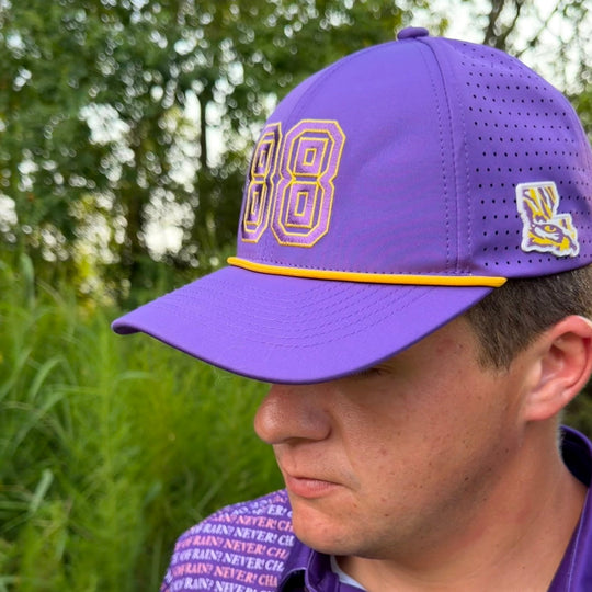 A man wearing a purple baseball cap with gold and white &