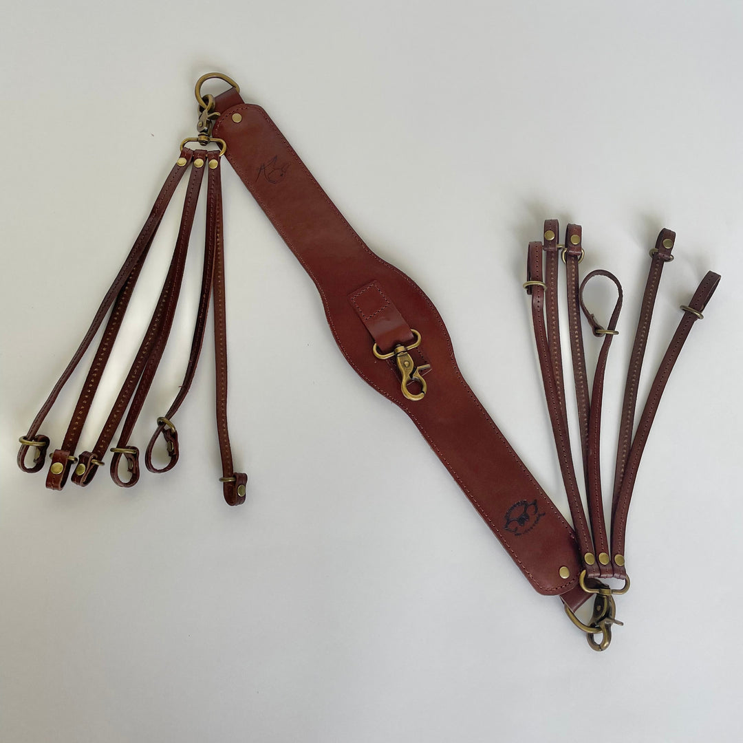 A reddish-brown leather duck strap set with brass hardware, laid out on a plain white background.