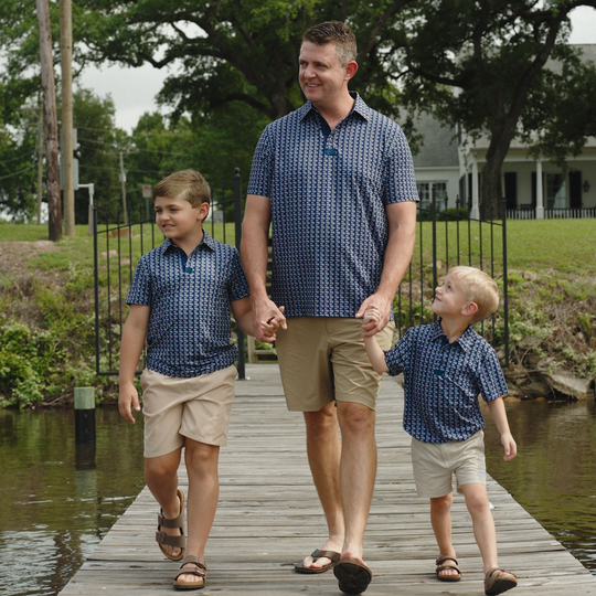 Man and two boys walking hand-in-hand on a wooden dock by a body of water.