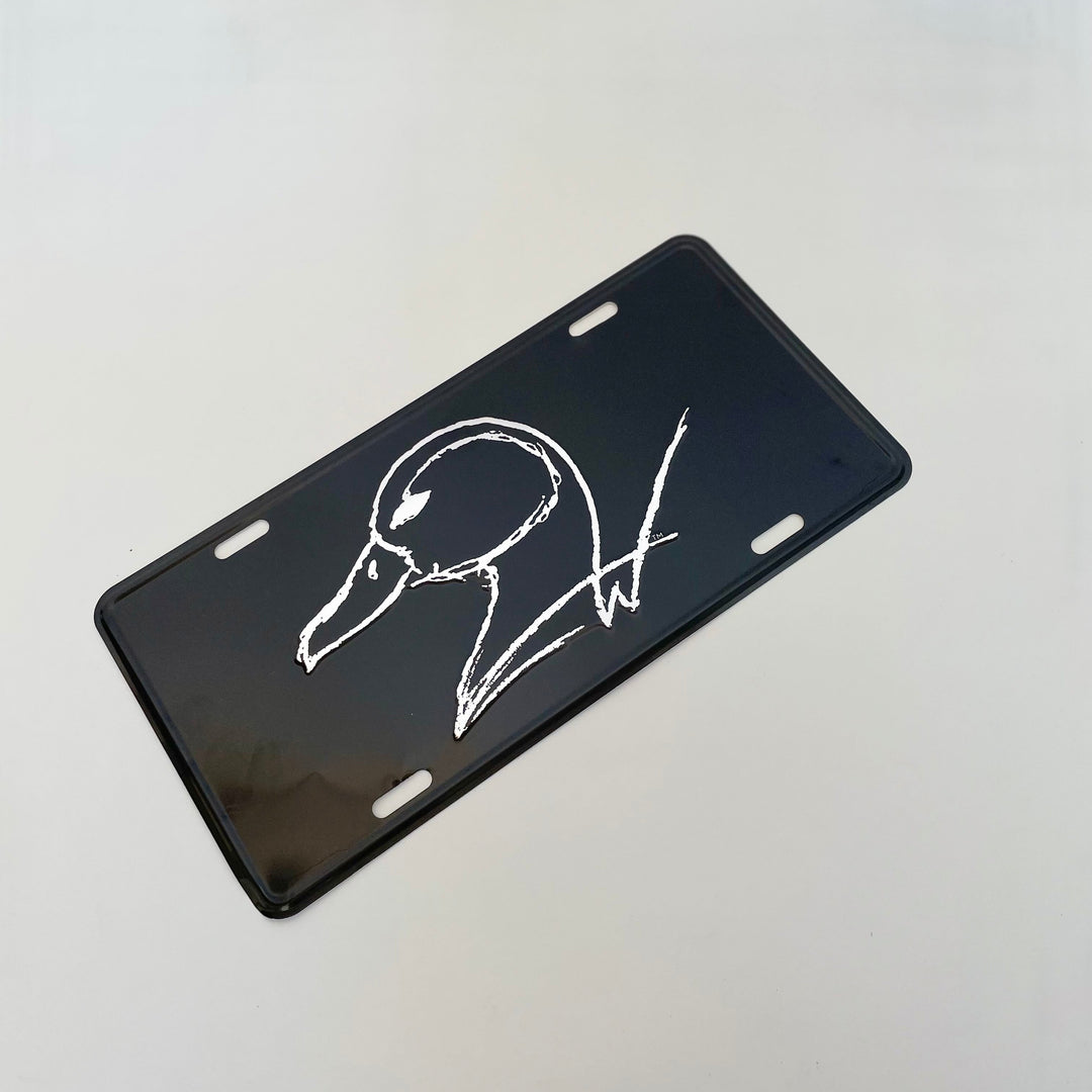 black vehicle license plate with silver etched duck logo on white background