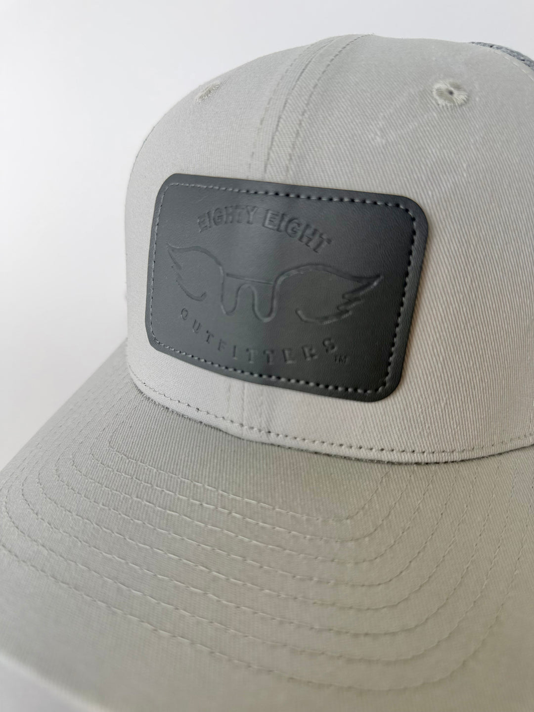 grey cap with a grey leather patch featuring a logo on a white background
