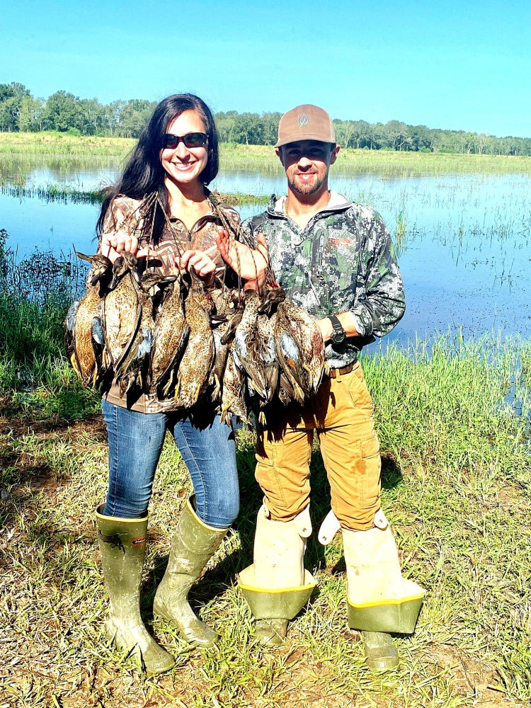 Two people holding hunted birds by a lake