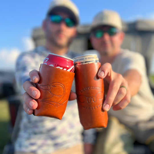 Two people holding leather can coolers with drinks, outdoors.