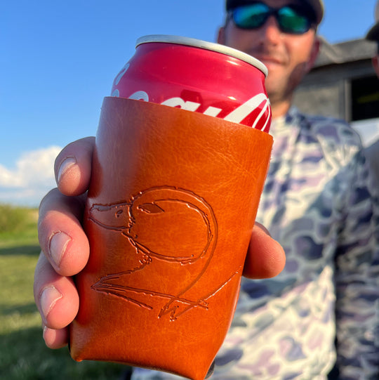 A brown leather can cooler with embossed designs with a man in the background