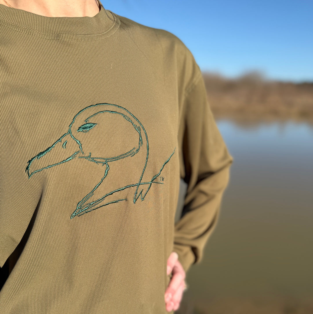 Person wearing a green sweatshirt with a duck design by a body of water.