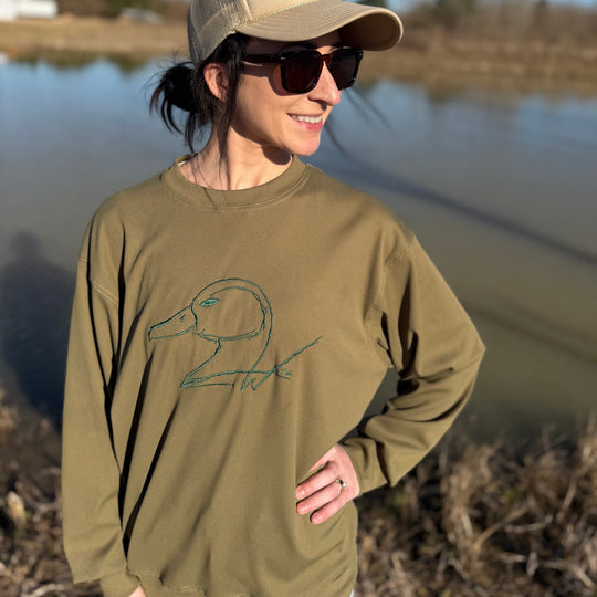 Person wearing a beige cap and sunglasses, standing by a body of water.