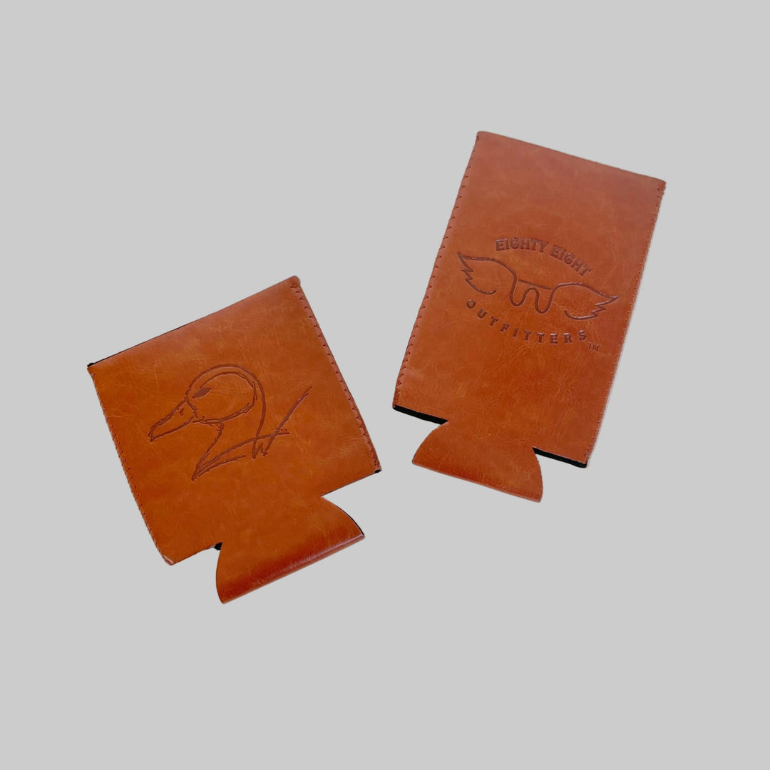 Two brown leather can coolers with embossed designs on a light gray background