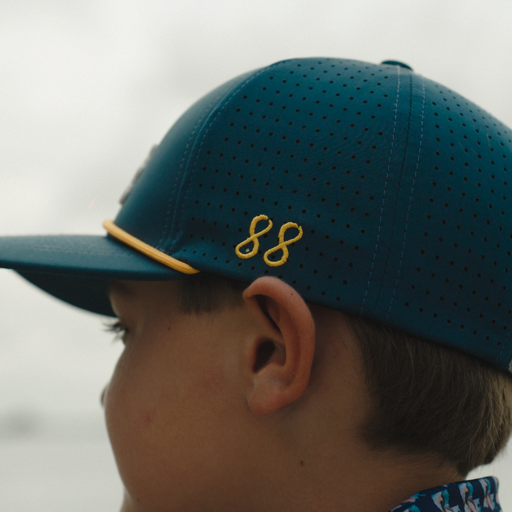 Close-up of a child wearing a blue cap with a yellow logo, looking away from the camera.