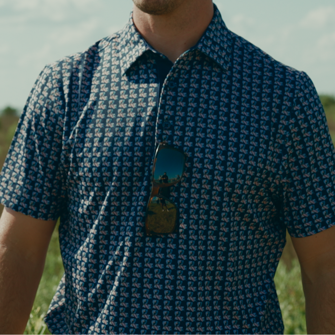 Man wearing a patterned shirt and cap standing in a field with a clear sky.