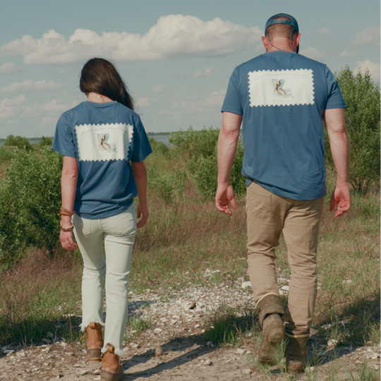 Two people walking on a dirt path in a natural setting with blue shirts and caps.