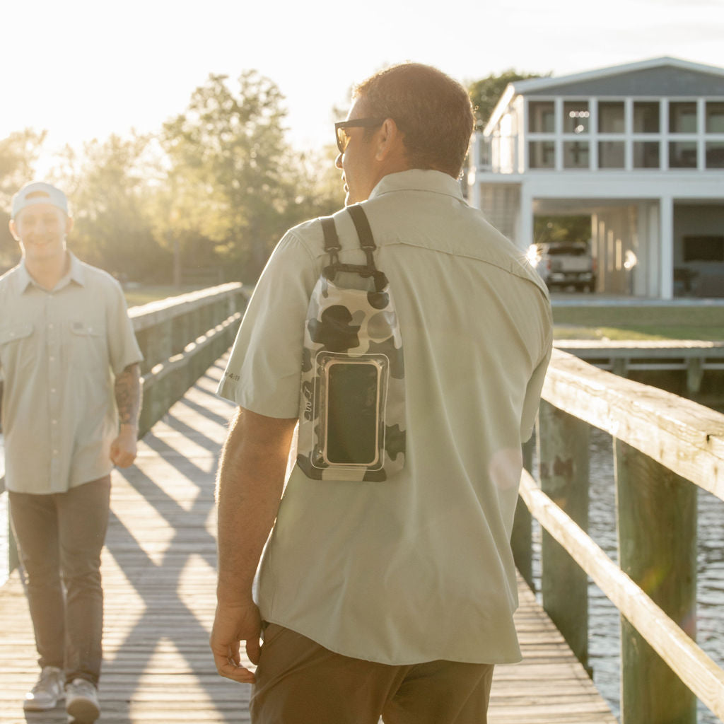 Person walking on a wooden dock wearing a light-colored shirt and carrying a backpack.
