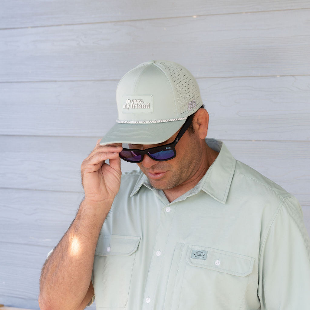 Man wearing a cap and sunglasses against a light wooden panel background