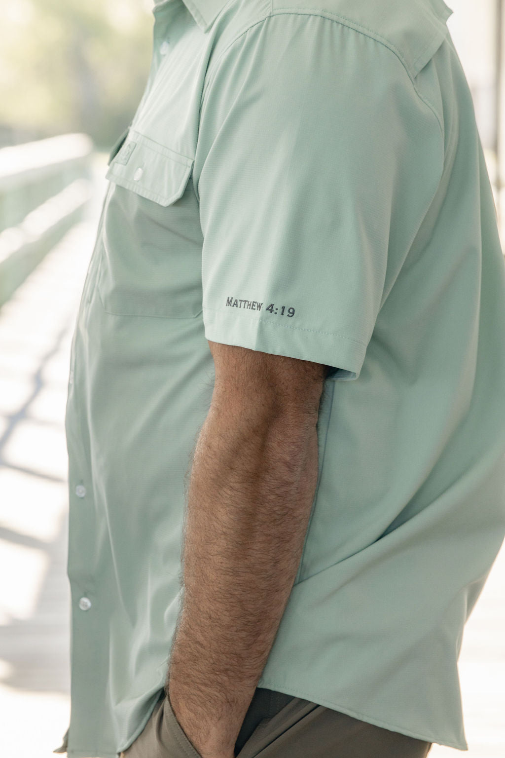 Light green shirt worn by a person with text on the sleeve, blurred background