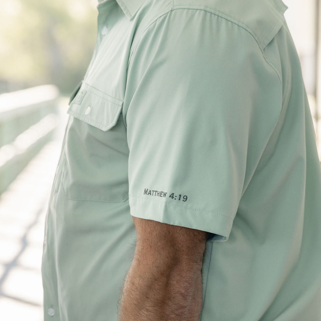 Light green shirt worn by a person with text on the sleeve, blurred background