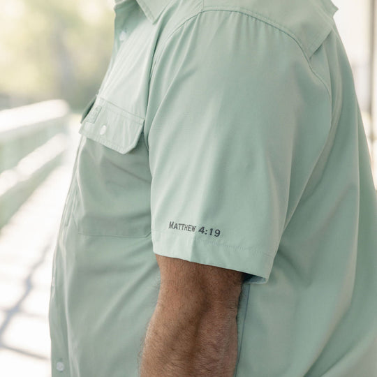 Light green shirt worn by a person with text on the sleeve, blurred background