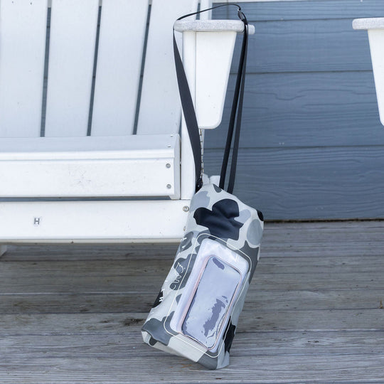 A gray and white camouflage waterproof phone pouch with a clear front window and black straps, resting on a weathered wooden deck next to a white chair.